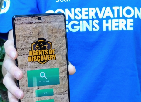 An intern holds a phone with the Agents of Discovery home screen open