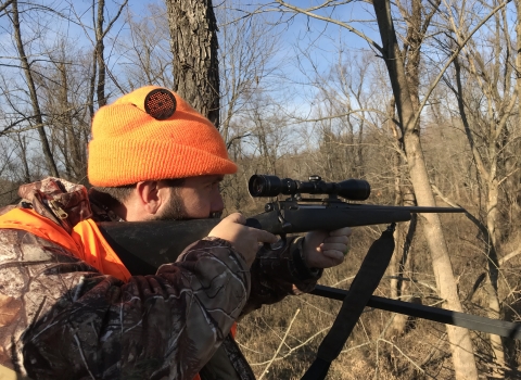 An image of a hunter in a tree stand with their rifle. 