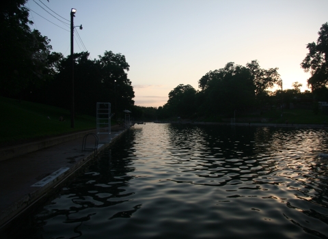 The pool at Barton Springs is shown against a sunset background.