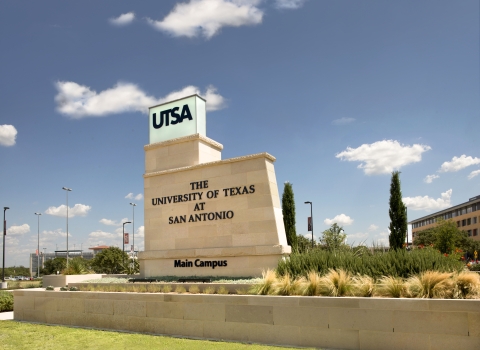 The main campus sign for the University of Texas at San Antonio is pictured in front of a blue sky.