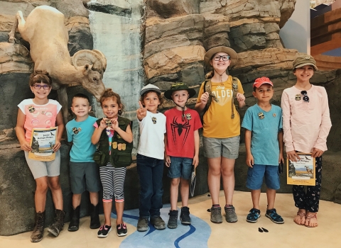 A group of youth standing in front of a faux rock wall. Some of the kids hold blue pastic badges