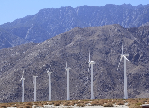 A row of wind turbines with mountains in the background.