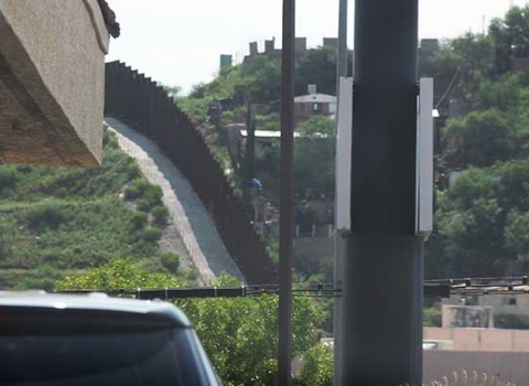 A tall wall is shown on a hillside representing the border between the United States and Mexico.