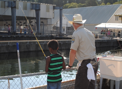 An adult showing a child how to fish looking over the railing at a fish hatchery.