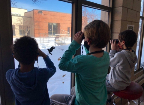 Children use binoculars at a window