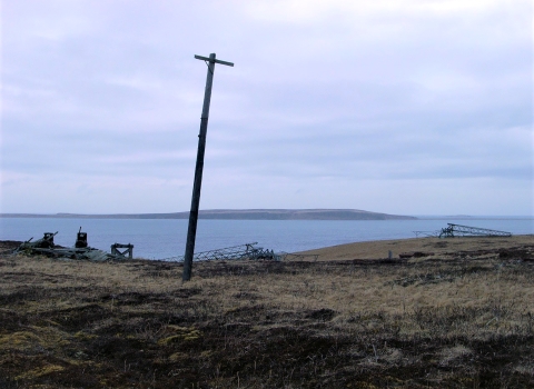 Abandoned equipment on an island: leaning electrical pole, fallen radio towers, and other debris.