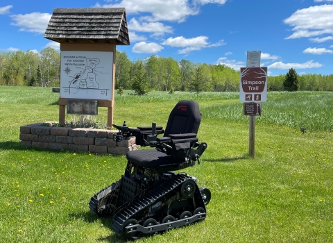 A tracked wheelchair in front of the Simpson Trail sign at Iron River National Fish Hatchery in Wisconsin.