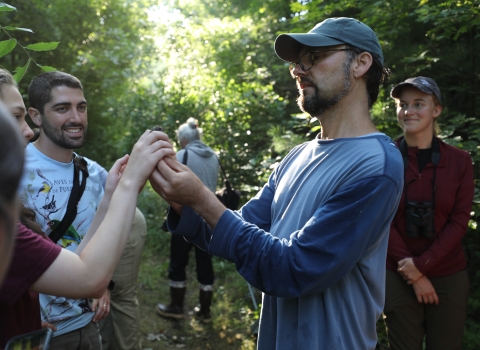 Biologist holds a small songbird up for a group of onlooking students
