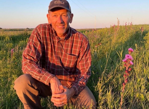 Craig Larson kneels on grasslands next to prairie flowers
