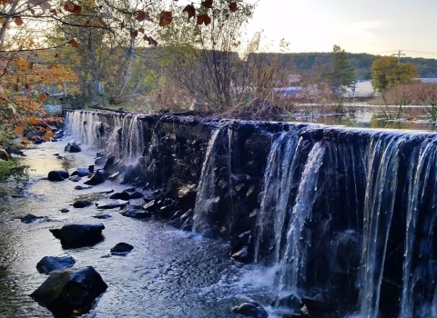 a waterfall pours over the edge of a dam against the backdrop of the city