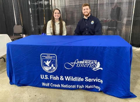 USFWS employee and volunteer sitting behind blue information booth