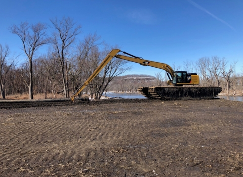 An excavator is moving dirt on an island of the river