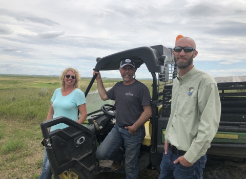 Jennifer and Chad Kunz with Curt Francis, all standing next to a utility vehicle on a grassland
