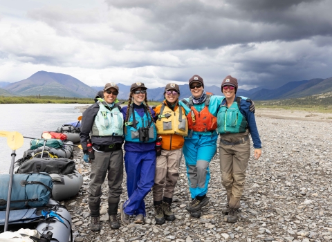 Five U.S. Fish and Wildlife Service employees pose for a group picture on the bank of a river with their rafts along the waterline.
