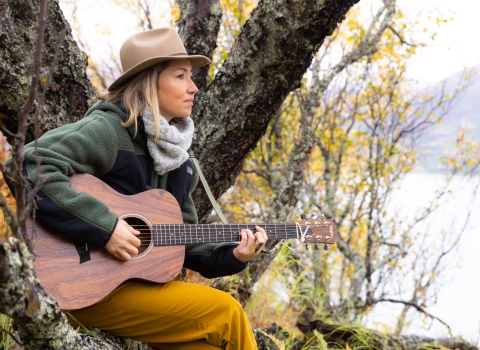A woman sits in a tree and plays guitar