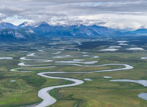 A river twists and turns across a plain bordered by snow-capped mountains.