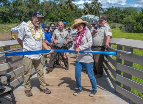 Pauline Kawamata from the Hawaiʻi Nature Center cuts the ceremonial ribbon at the rededication ceremony. USFWS staff and event attendees stand behind. 