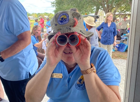 Volunteer looks through carboard binoculars at camera.