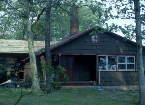 A dark brown cabin with red trim exhibits damage from a tree fall.