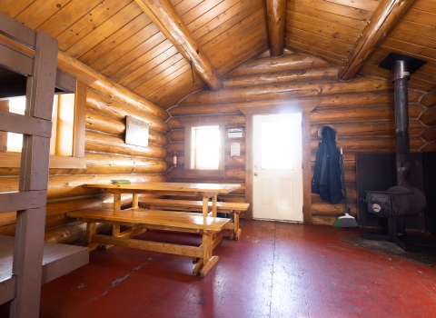 Inside of a log public use cabin with table, woodstove, and bunks.
