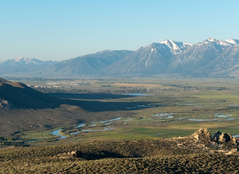 A view of the Carson Valley during sunrise. Mountains are off in the distance while a river cuts through the sagebrush filled valley below.