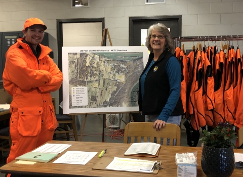 Lowell Haagenson and Lori Bennett inside the NCTC deer check-station surrounded by hunting area maps and blaze orange vests for hunters. 