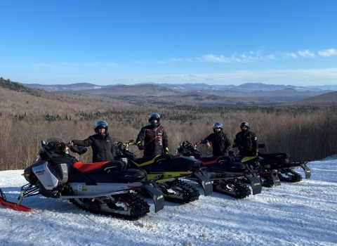 People on snowmobiles post on a trail that overlooks the mountains in Vermont