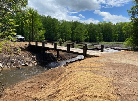 A bridge over a free-flowing creek with burlap covered soil for replanting on the banks
