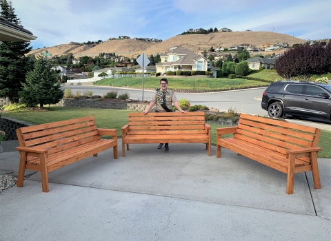A youth volunteer in his boy scout uniform poses behind the wooden benches he  made for Leavenworth NFH