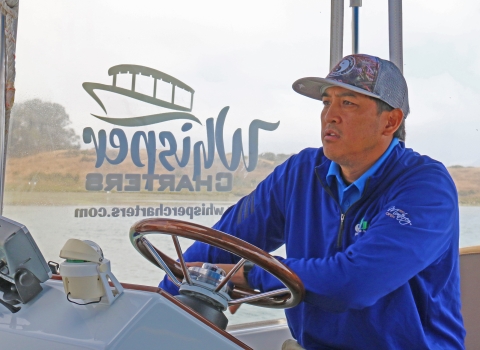 A man wearing a blue jacket driving a boat
