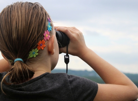 A young woman looking through binoculars along a railing