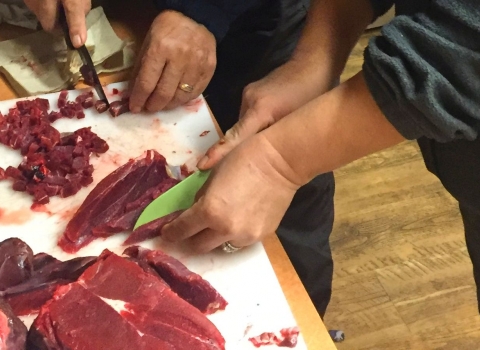 Red caribou meat being cut into slices and cubes on a kitchen table