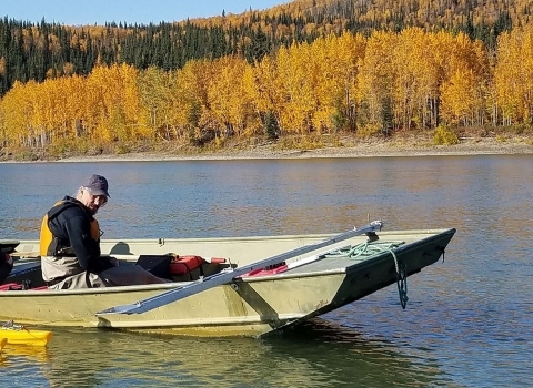 Two men in a small motorboat assessing water quality on a river in fall