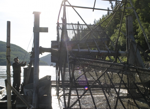 man standing on a fish wheel platform in a large river