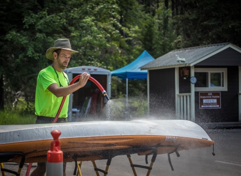 A man uses a hose to wash off the bottom of a kayak