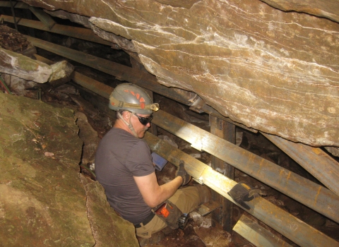 A man in a hard hat builidng a wooden barrier inside a cave.