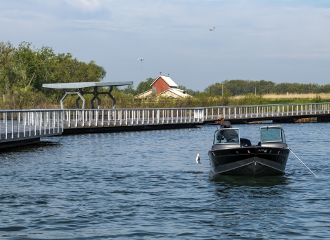 Looking straight at a fishing boat catching a white bass with fishing pier along left side and visitor center in background on a sunny day