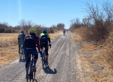 cyclists ride along a dirt road in the desert