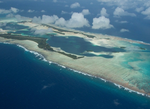 Aerial view of an island atoll surrounded by sandy reef in the deep blue ocean