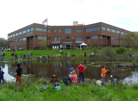 People fishing on a pond in front of a large brick building. Text on building U.S. Fish and Wildlife Service