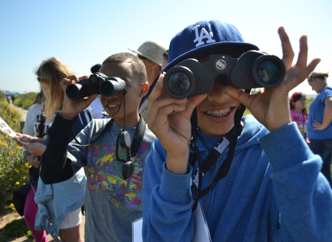 Smiling children look through binoculars on a sunny day.