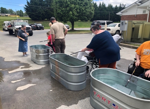 People fishing out of small, galvanized stock tanks in a parking lot