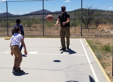 2 kids and adult play basjetball on outside court