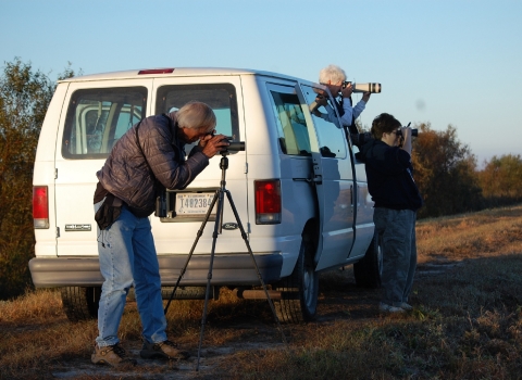 3 people using scopes & binoculars by white van looking for wildlife