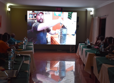 class watches man on video screen with what looks like metal jug