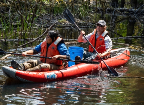 Service intern, Suzena Arias, and employee rafting through wetland to check minnow traps