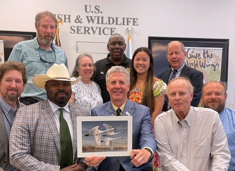 A group of people pose with the winning artwork depicting trumpeter swans.