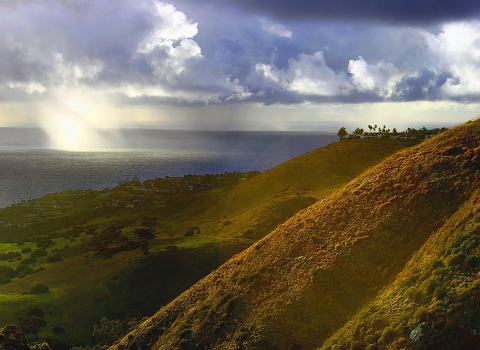 vegetated land sloping towards the Pacific Ocean with rays of sunlight appearing through clouds
