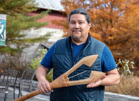 up close image of man holding wooden spear with fall leaves in background