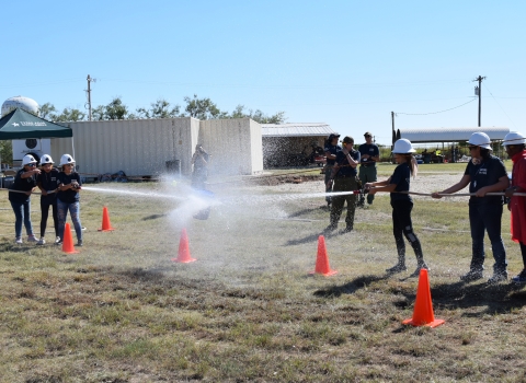 2 groups of people face ech other holding fire hoses whose spray hits the other